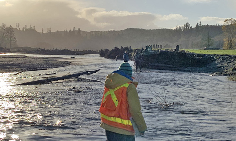 person in construction vest standing beside a flooded river bank