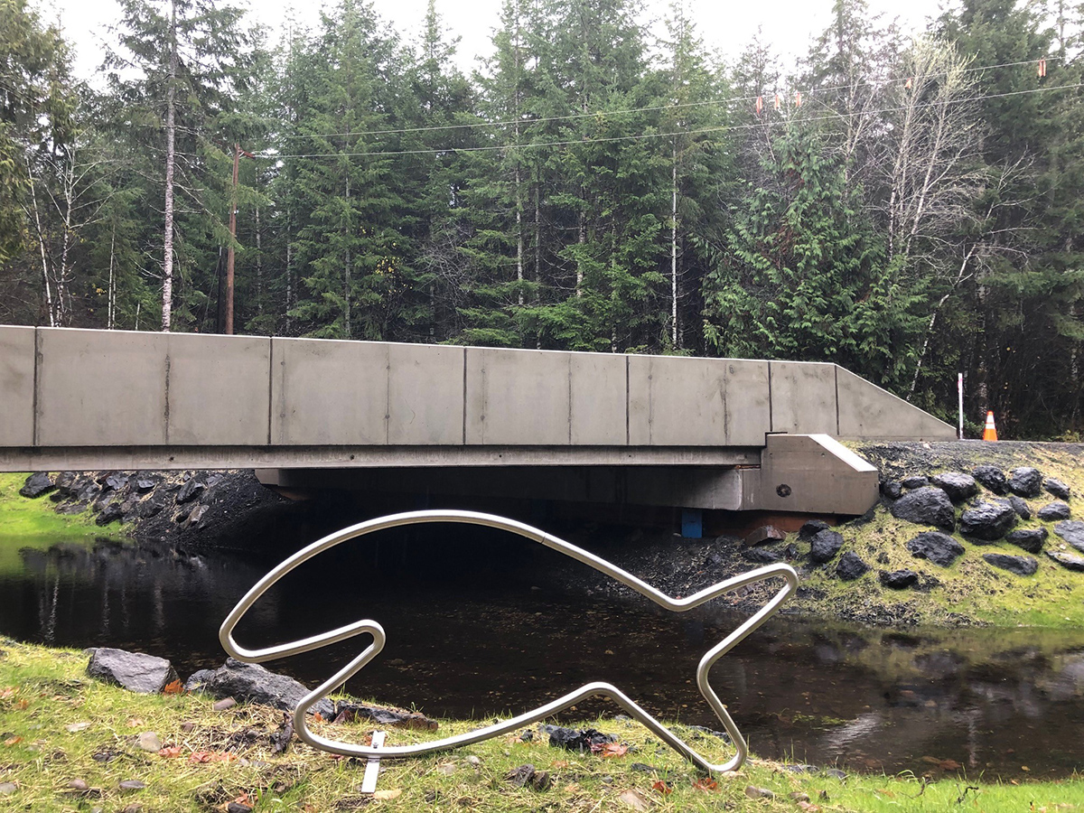 After photo showing the change at the Wildcat Creek County Line Road Fish Barrier Correction project. The first photos shows undersized culverts beneath the road. The second photos shows a channel-spanning bridge with the traveling metal Happy Fish sculpture.