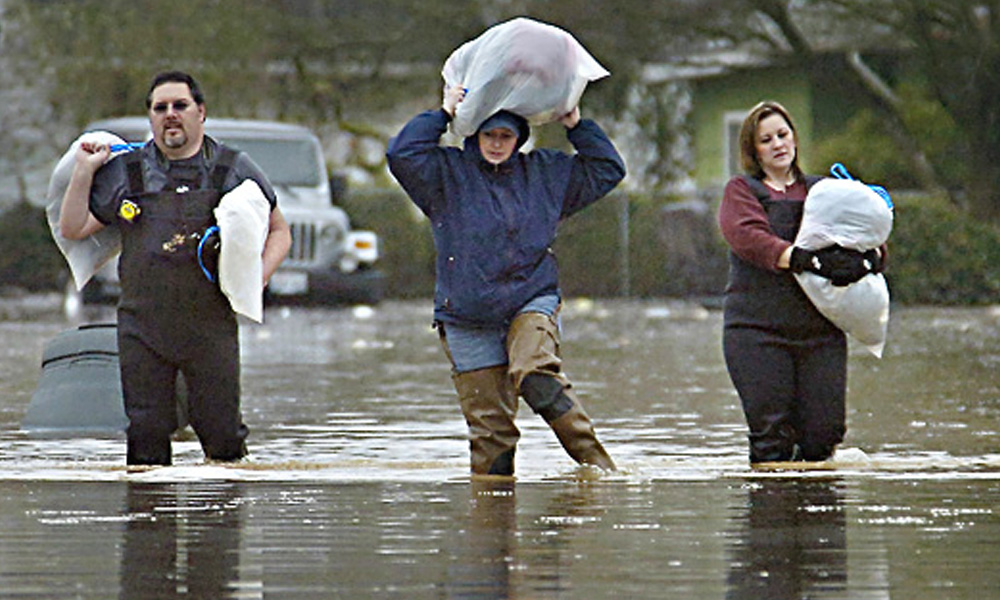 Three people walking in a flooded area with their belongings in bags overhead
